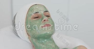 水疗沙龙的女人。 口罩。 美丽的女孩躺在沙发上，戴着绿色面具躺在美容诊所里